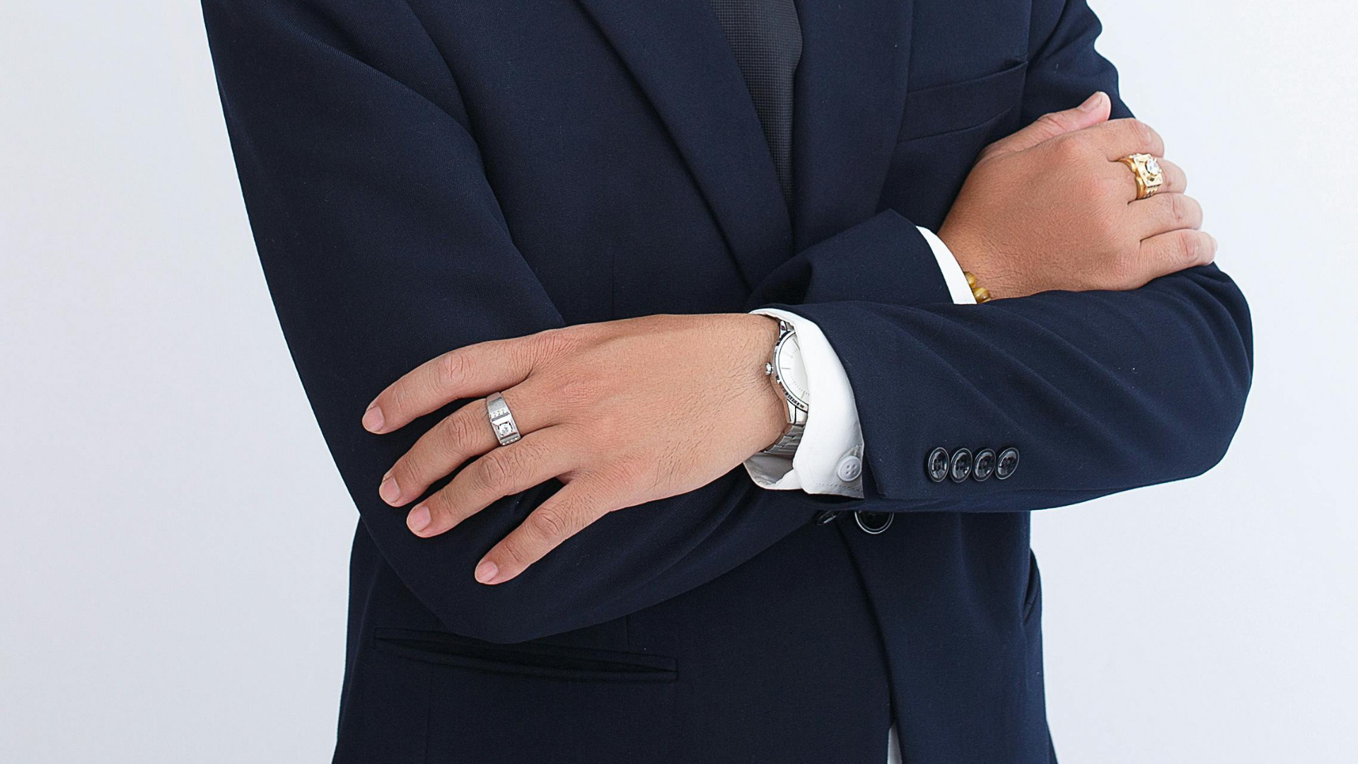 ネイビーのスーツで腕を組む男性の手元（腕時計と指輪を着用）