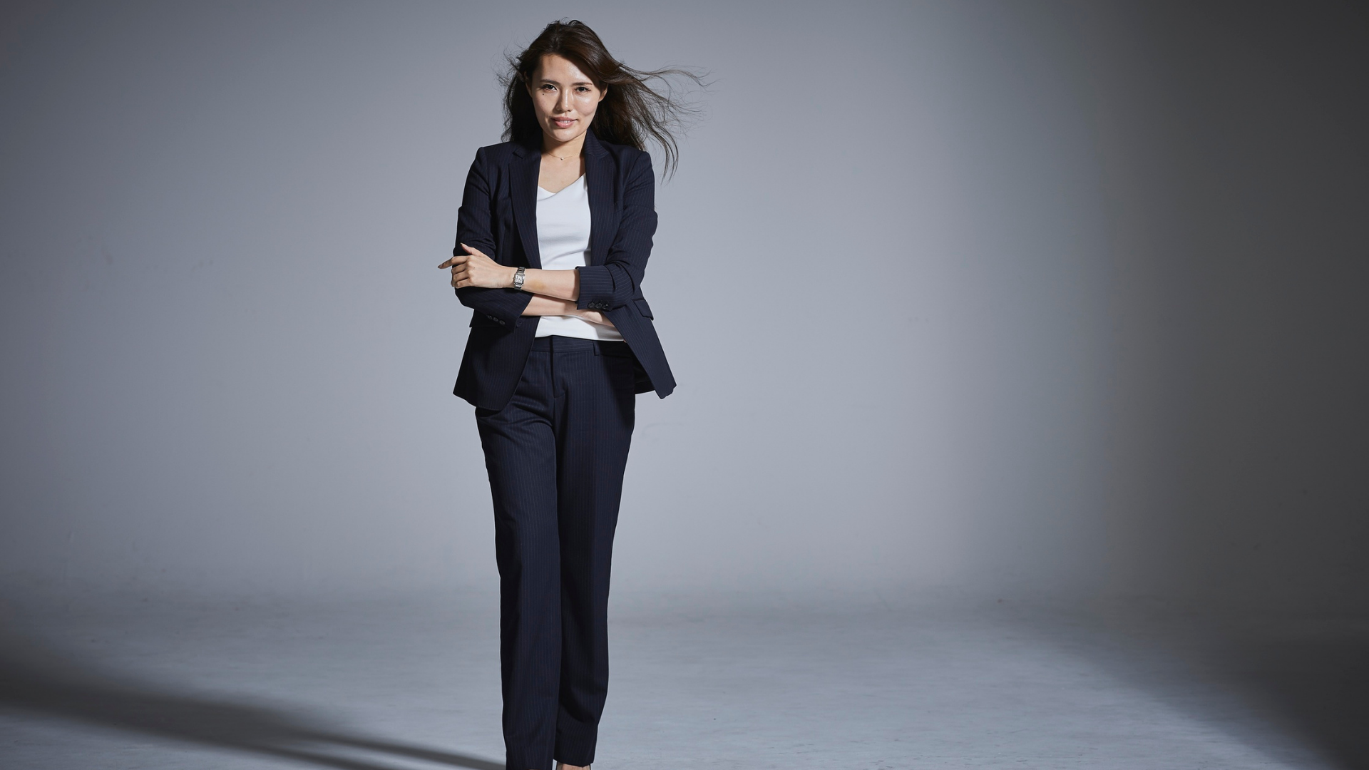 ネイビーのパンツスーツを着て腕を組んで立つアジア人女性